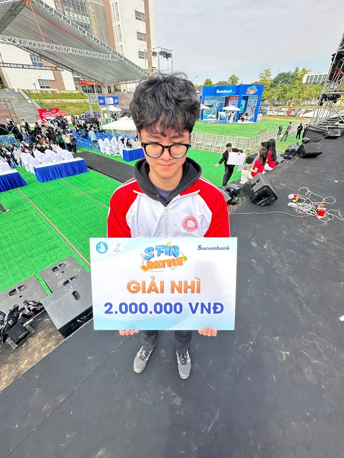 Holding the second-prize board at S-Fin Battle, on the stage apron with the campus behind